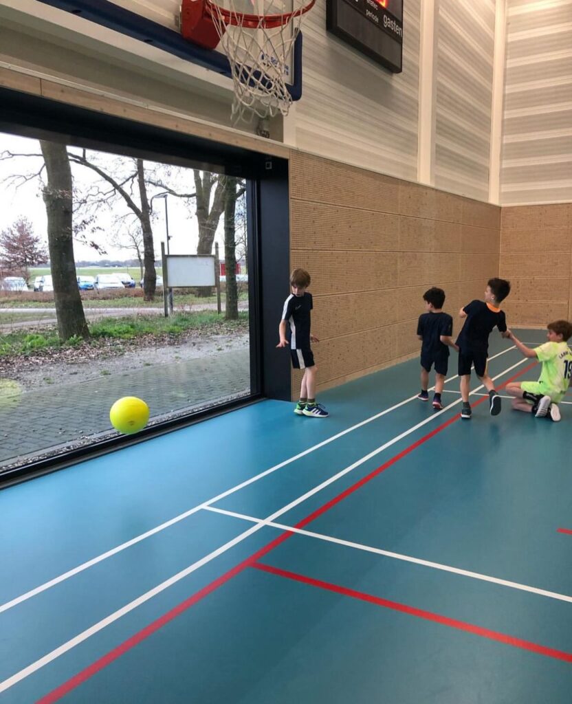 Kinderen voetballen in de gymzaal bij Sport-BSO Flekss